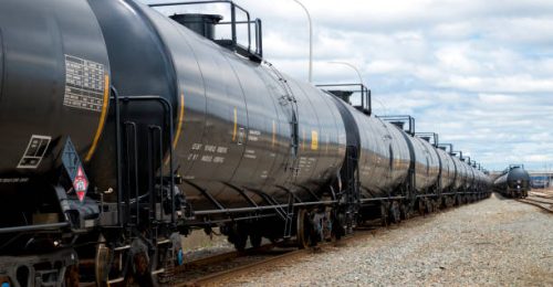 Black railway tanker cars of the type used to transport petroleum products. Several cars visible on two separate sets of tracks. Identification markings have been removed, only technical infomation remains.